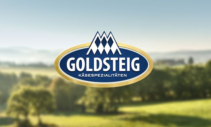 Logo GOLDSTEIG Käsespezialitäten, im Hintergrund Landschaft mit Wald und Wiesen